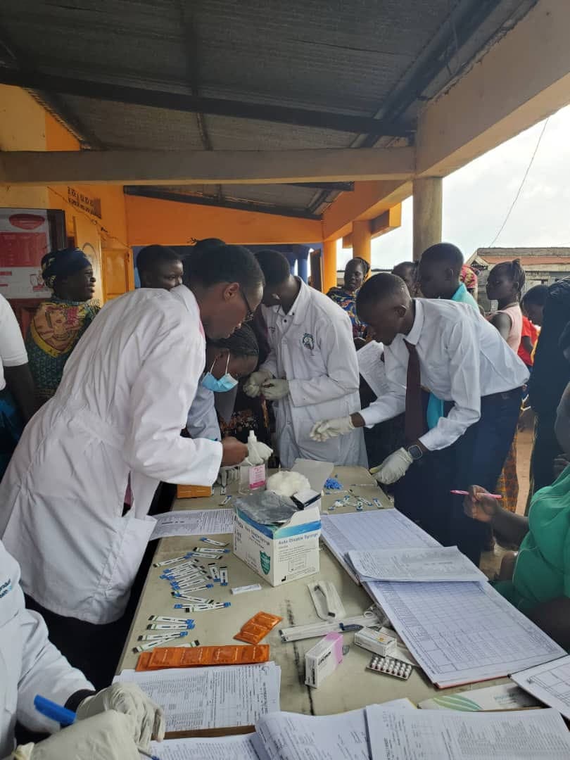 Clinicians in white coats working at an outreach table laid out with syringes, contraceptives and paper registers, with women and young people waiting on the other side.